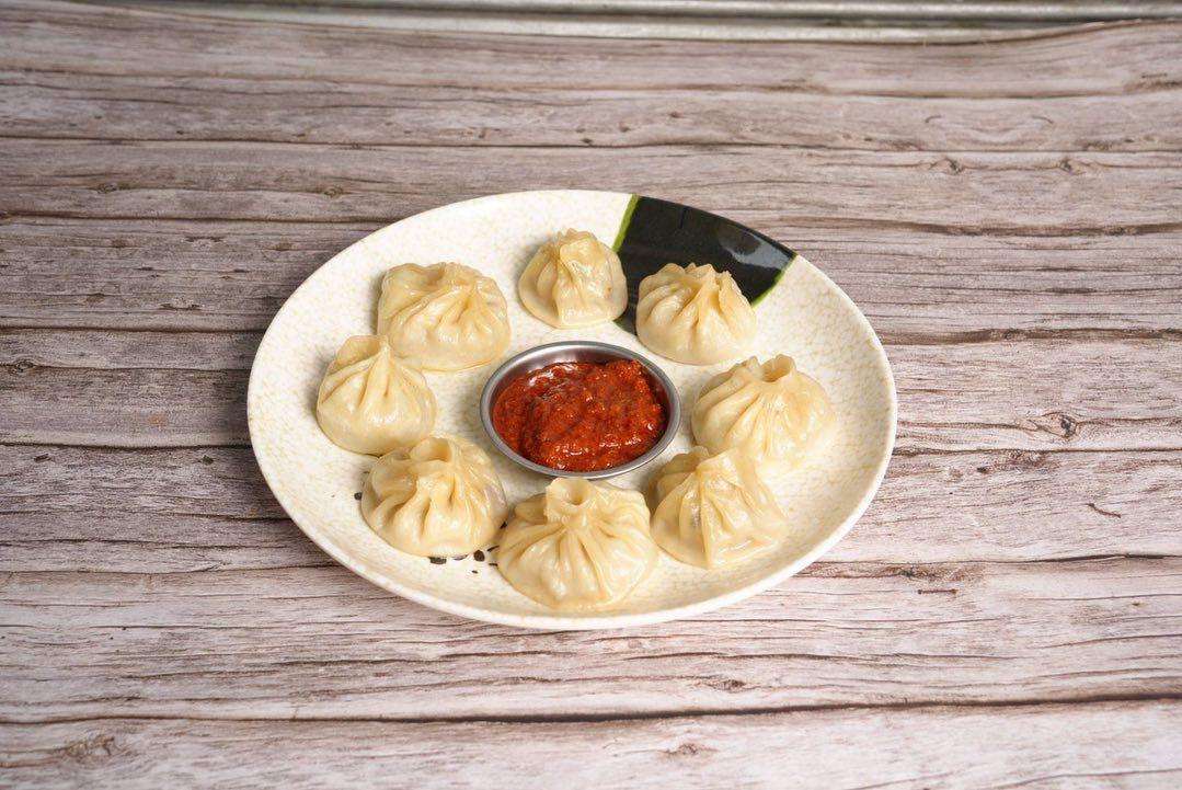 Steamed Chicken Momo on a white plate against a wood background