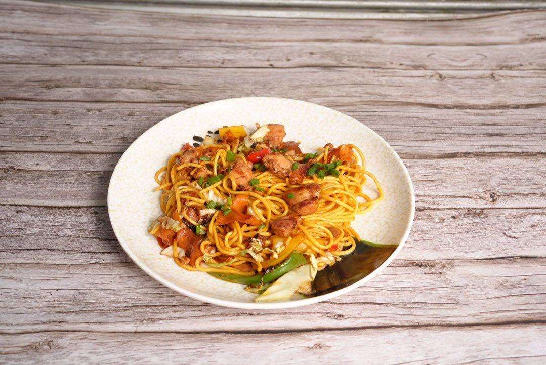 Chowmein on a white plate against a wood background.