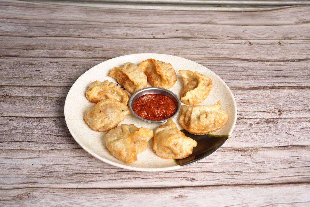 Fried Beef Momo with spicy red sauce on a white plate against a wood background