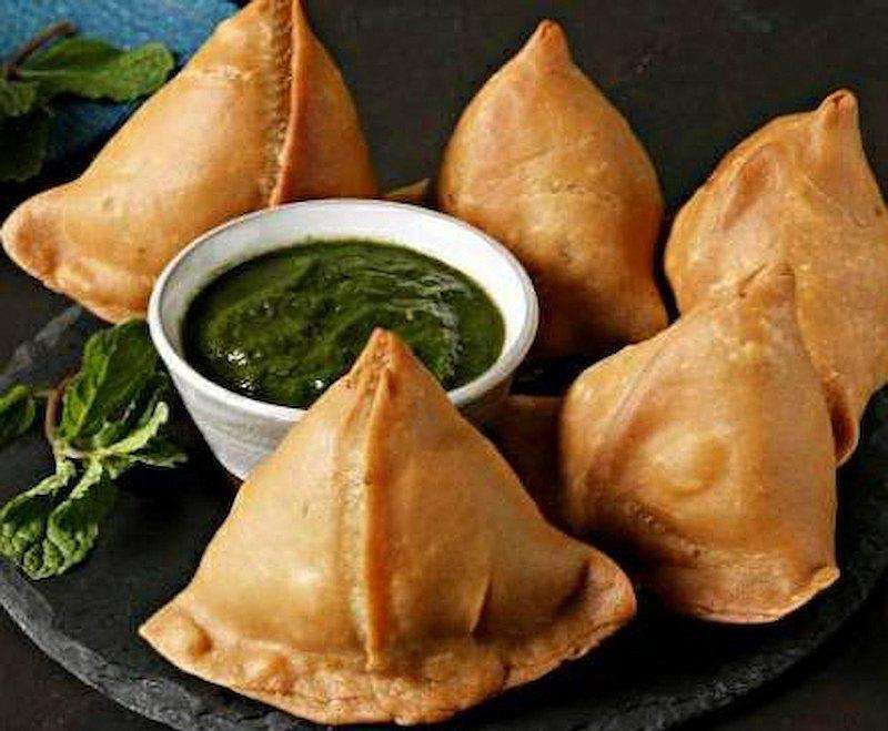 Samosa served with green sauce on a dark plate against a dark background