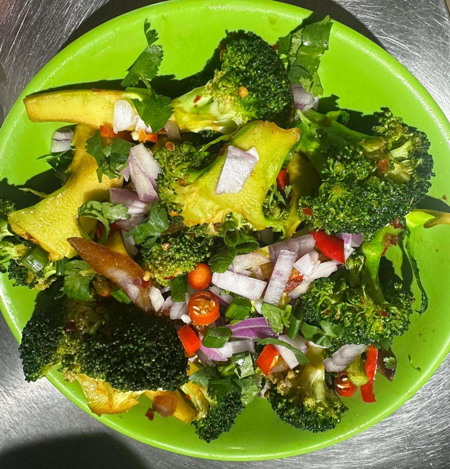 Spicy Broccoli served with fresh veggies on a green plate against a metal background.
