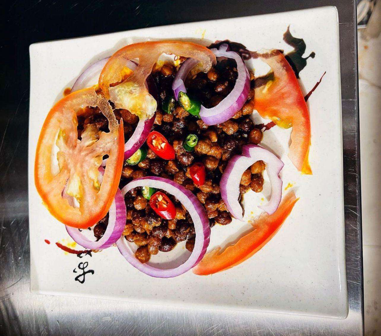 Spicy Chili chana served with fresh tomatoes and onions on a white plate and a metal background.