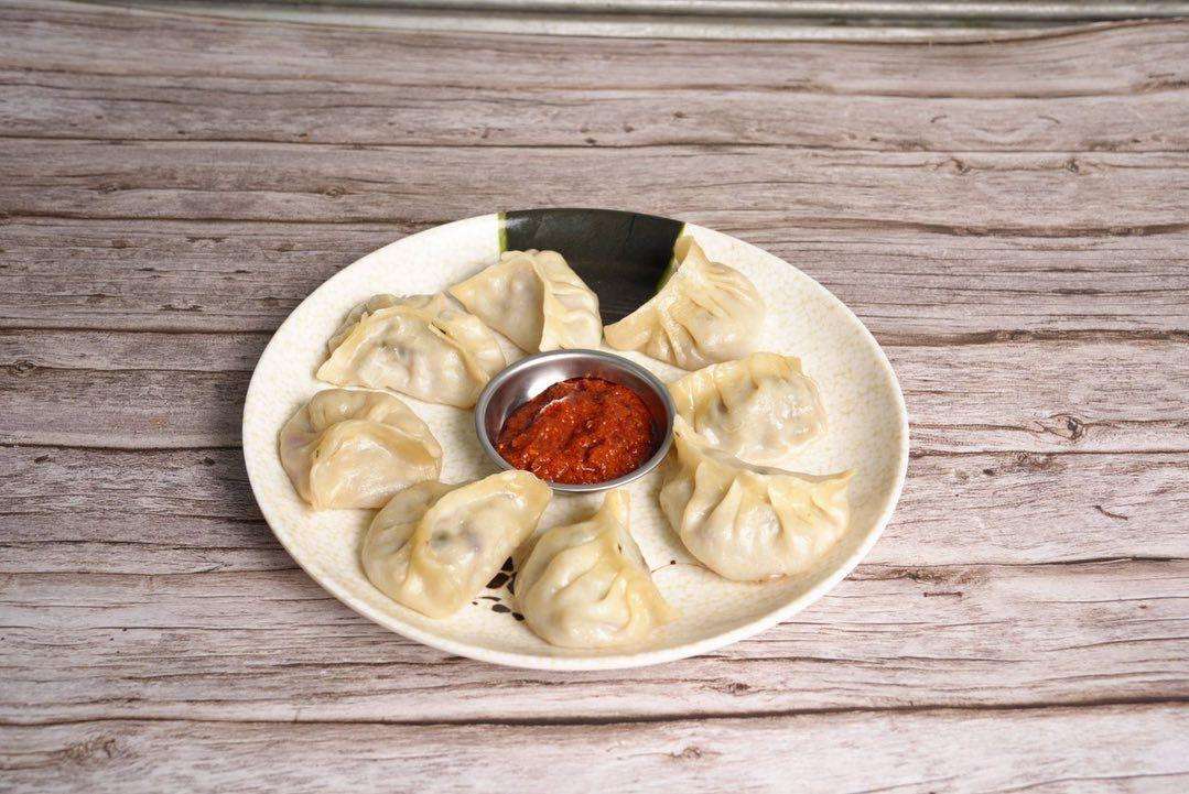 Steamed Beef Momo with a red sauce on a white plate against a dark background.
