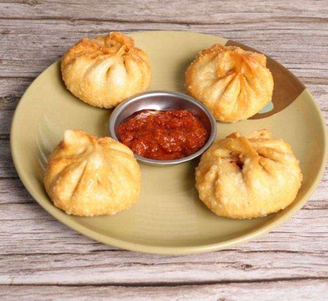 Taipo Momo with red spicy sauce, on a brown plate against a wood table background.