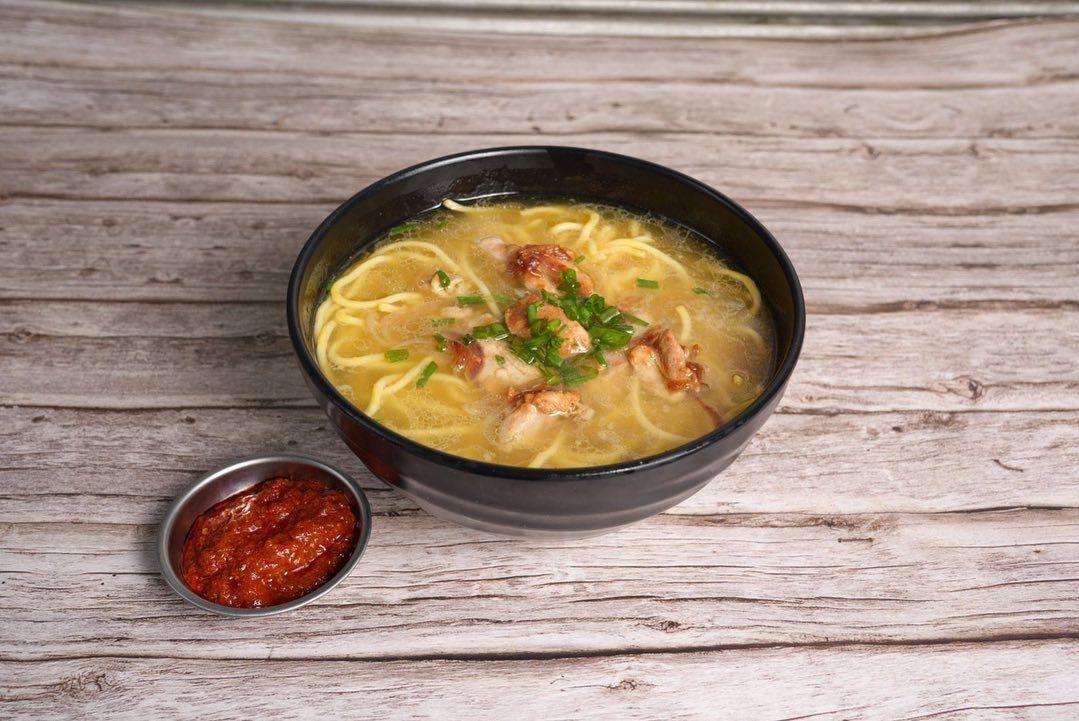 Chicken Tibetan Thukpa in a black bowl served with spicy red sauce in a metal slider on a wood background.