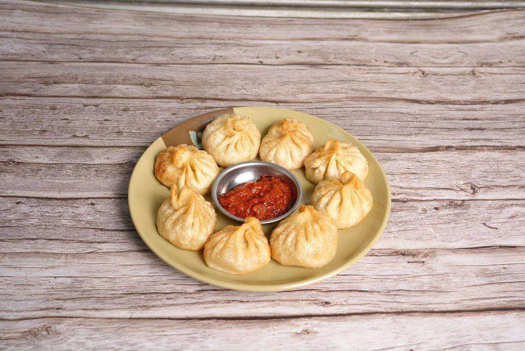 Fried Veggie Momo with spicy red sauce on a brown plate against a dark background.
